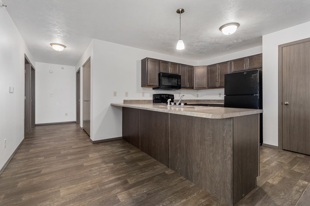 A kitchen with a wooden floor and a black fridge.