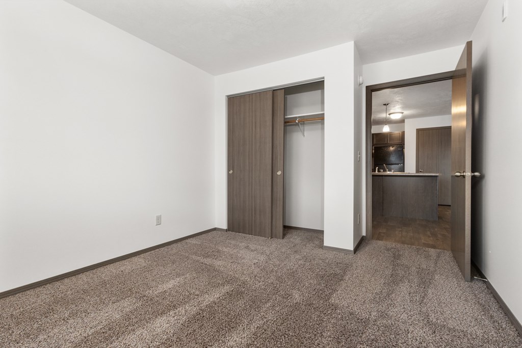 A room with a carpeted floor and a doorway leading to a kitchen.