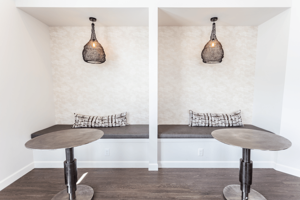A room with a bench and a table with a lamp on top.