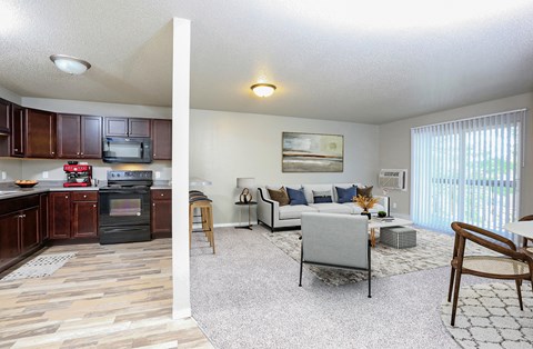 A living room with a grey couch and a kitchen area with brown cabinets.