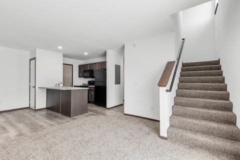 a living room with stairs and a kitchen with a refrigerator