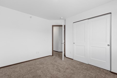 a bedroom with white walls and carpet and a door to a closet