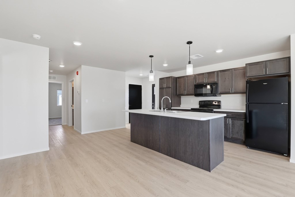 A kitchen with a black fridge and microwave, brown cabinets, and a white countertop.