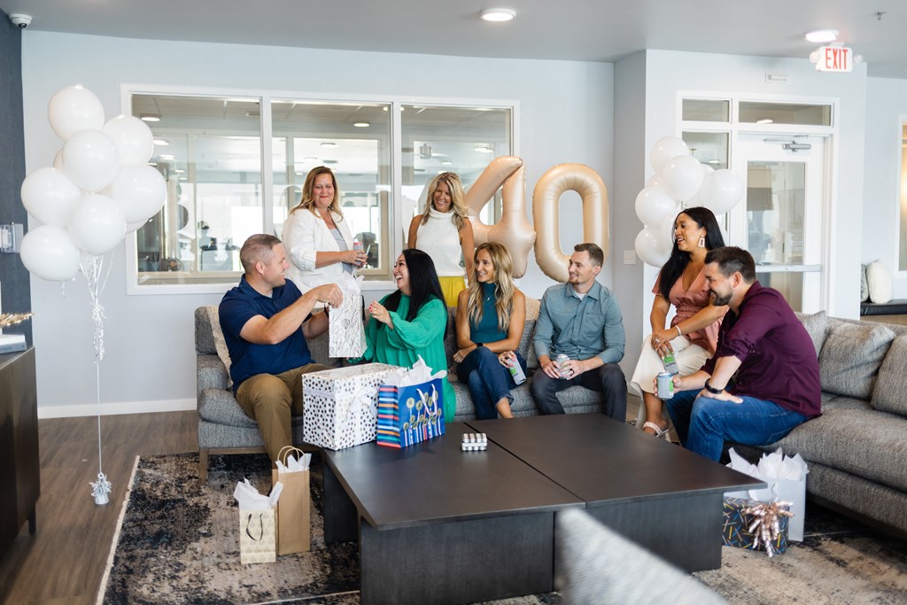 a group of people sitting in a living room with balloons and a 020 sign
