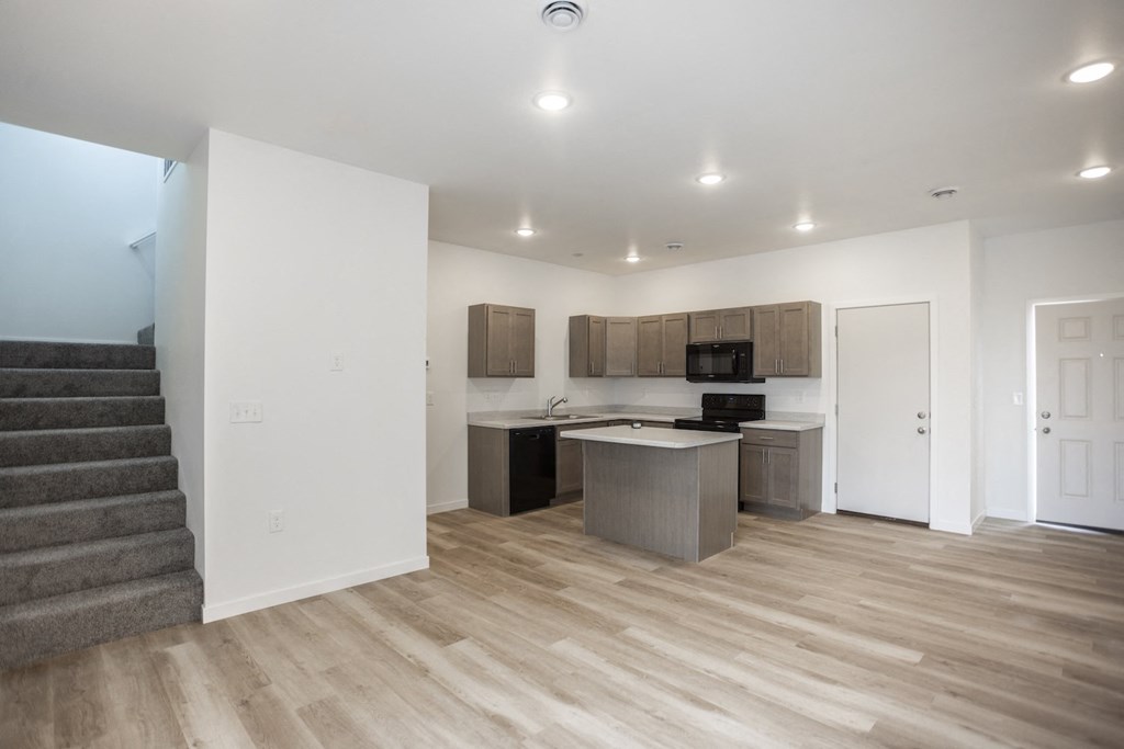 an empty living room with a kitchen and stairs
