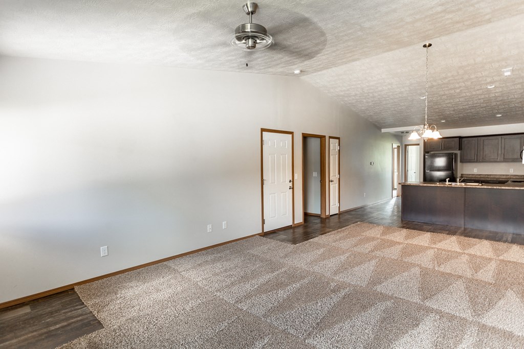 an empty living room with a kitchen and a ceiling fan