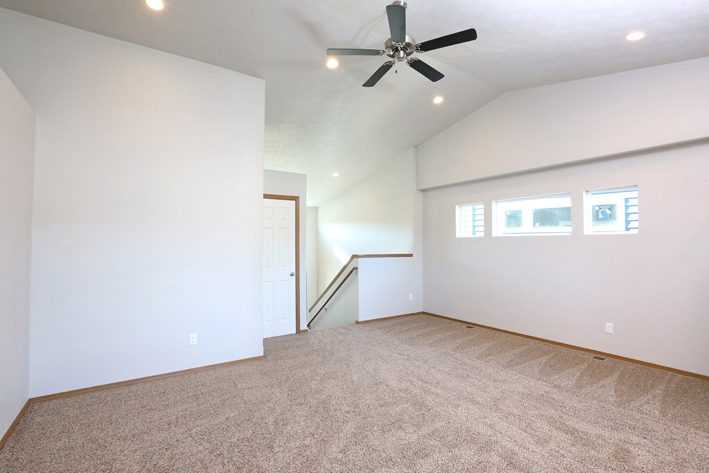 an empty living room with a ceiling fan and white walls