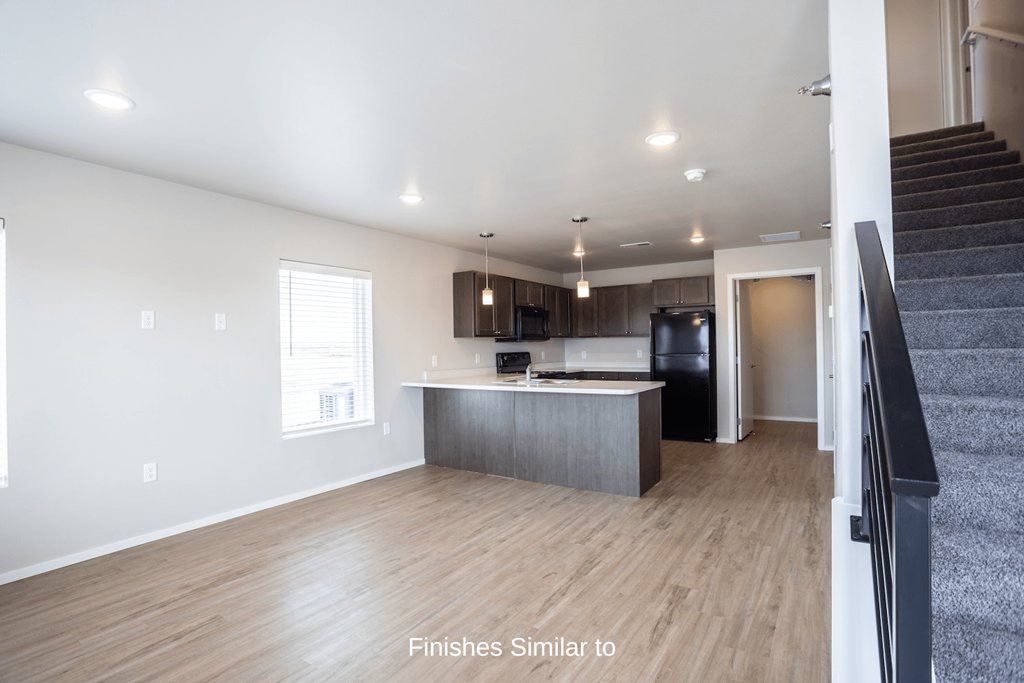 an empty living room with a kitchen and stairs