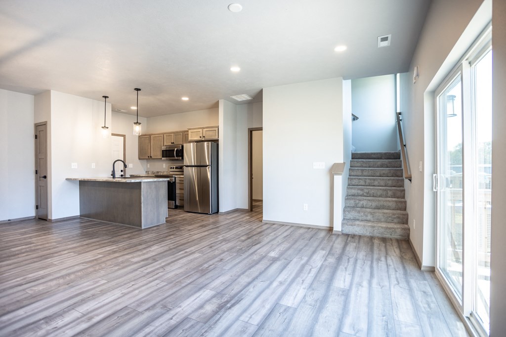 an empty living room with a kitchen and stairs