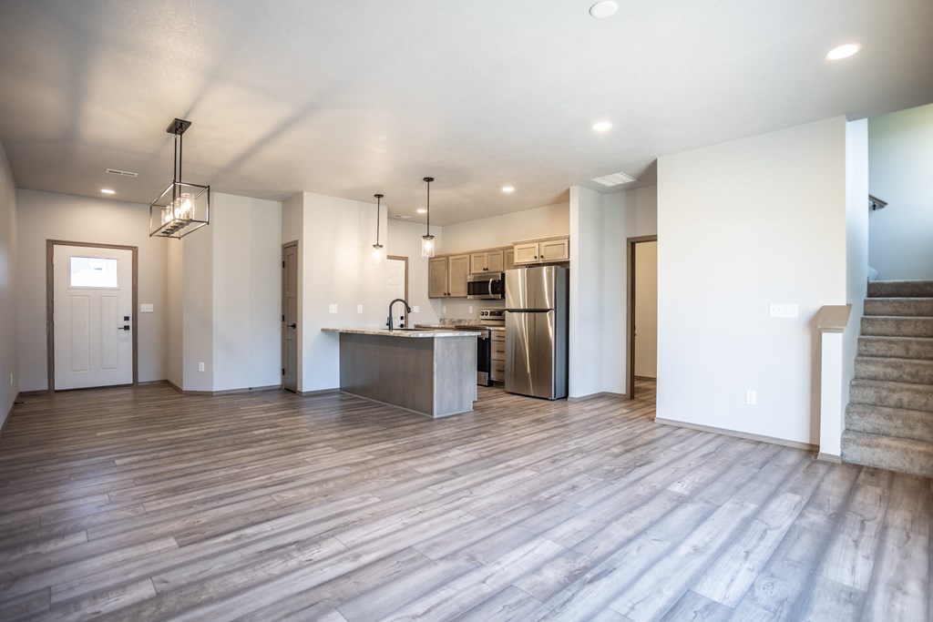 an empty living room with a kitchen with a stainless steel refrigerator