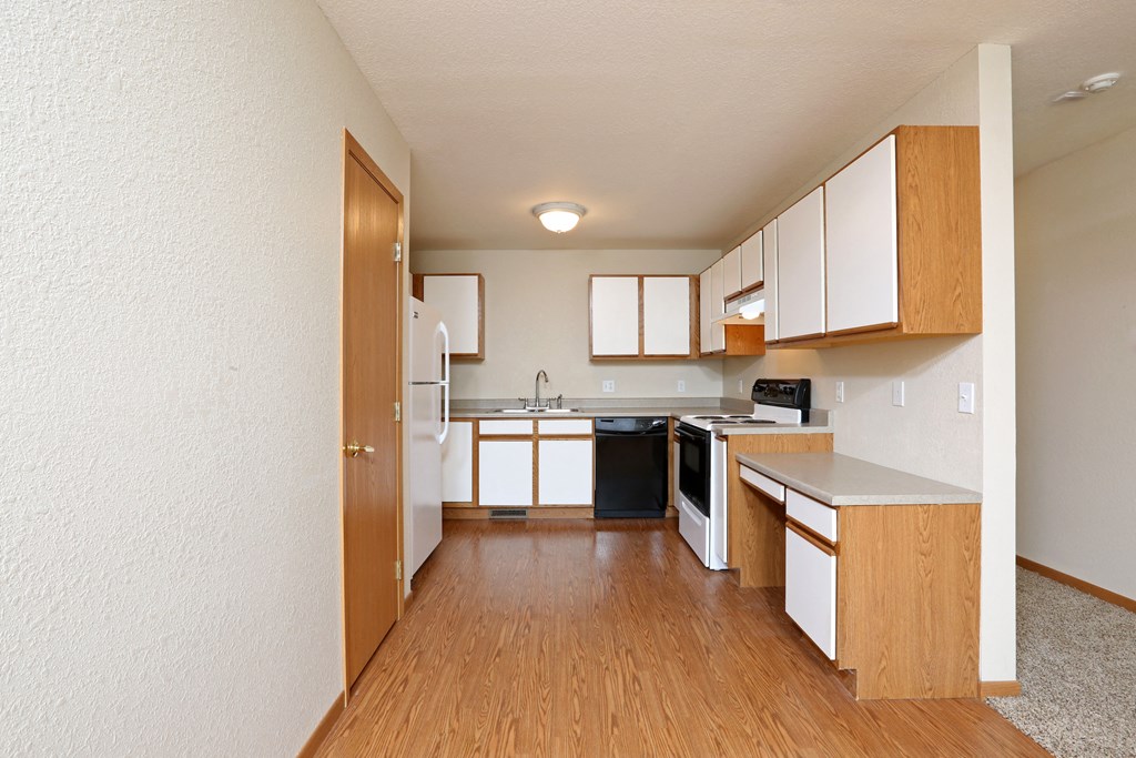an empty kitchen with wood flooring and white cabinets and