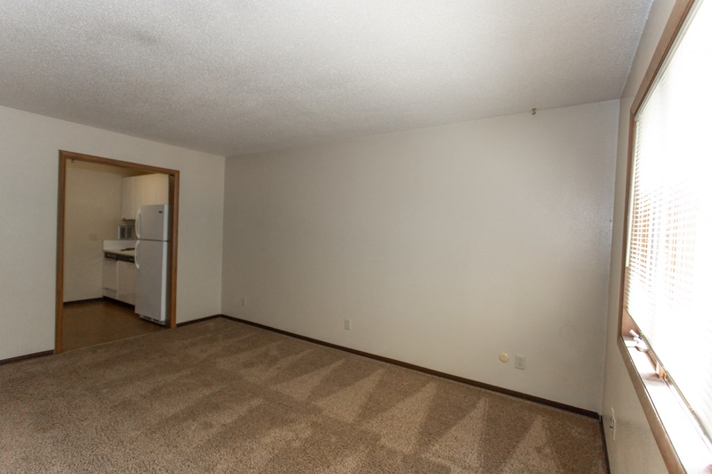an empty living room with carpet and a door to a kitchen