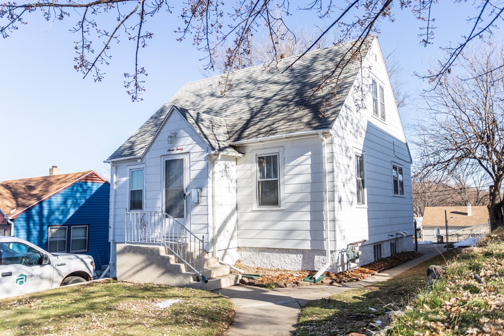 a white house with a gray roof and a blue house behind it