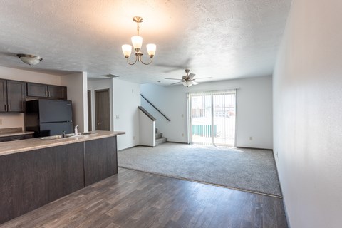 an empty living room with a kitchen and a ceiling fan