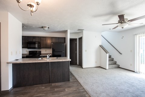 an empty living room with a kitchen and a ceiling fan