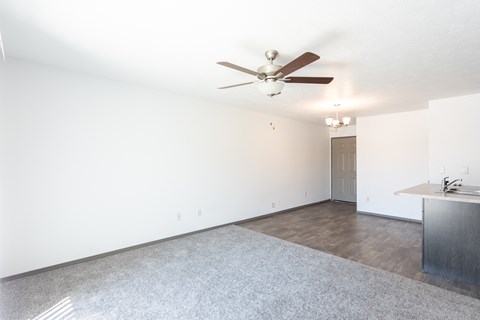 an empty living room with a ceiling fan and a kitchen