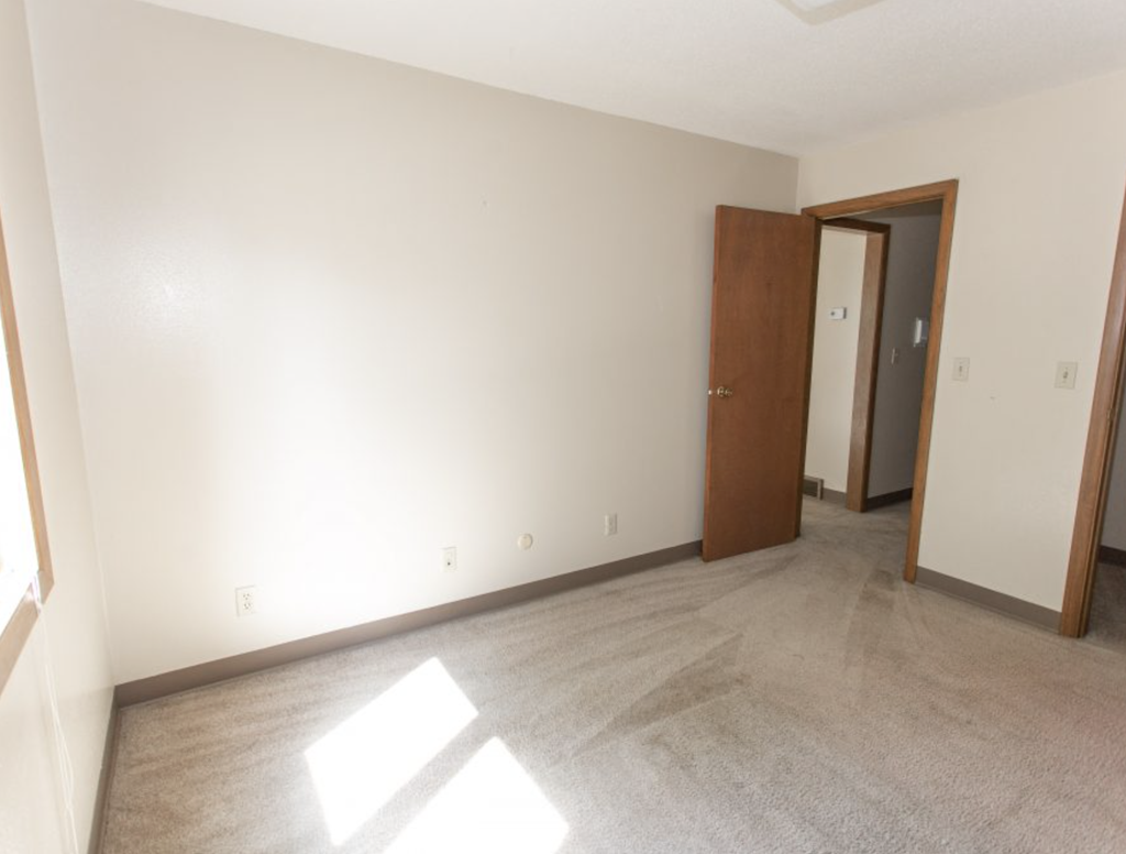 an empty living room with white walls and a door to a bedroom