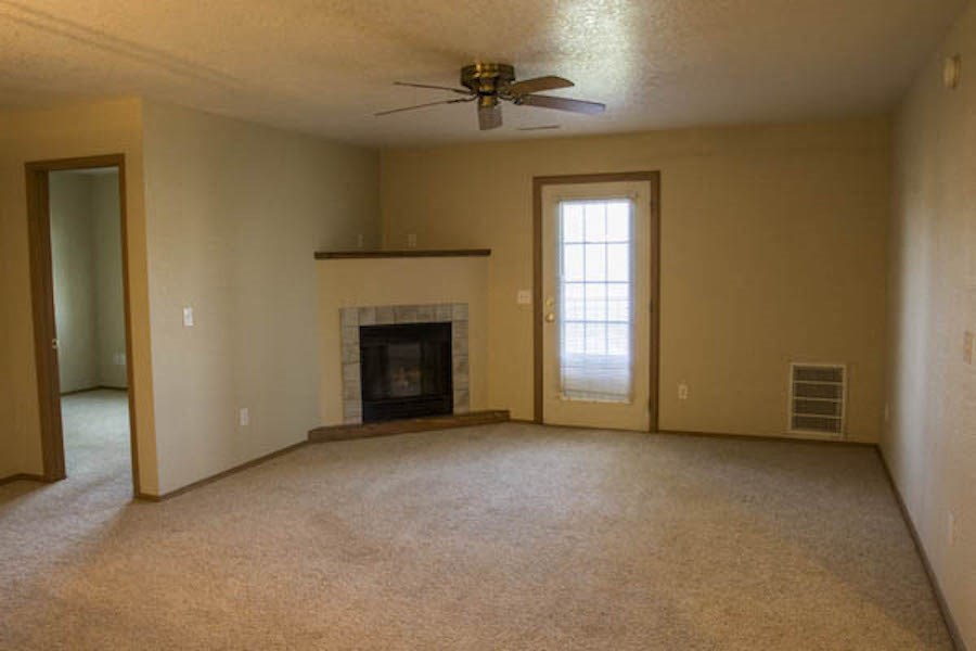 an empty living room with a fireplace and a ceiling fan