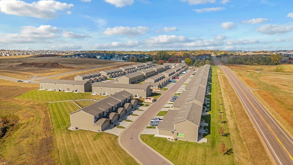 A large, modern building complex sits in a grassy field with a road running in front of it.