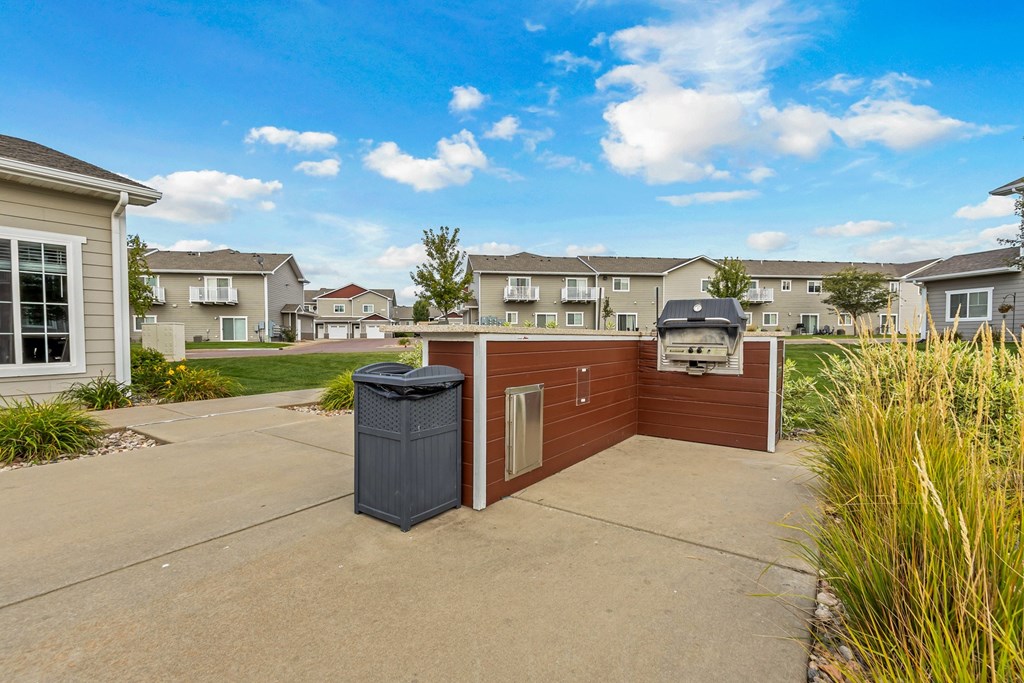 A residential area with a brown house and a grey trash bin.