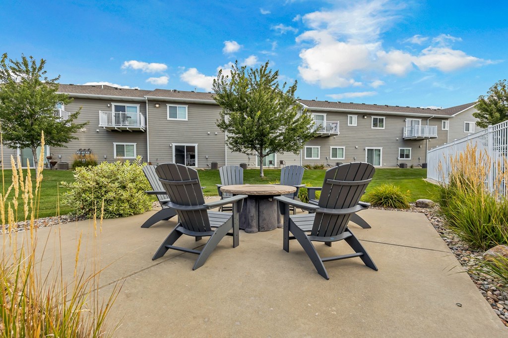 A concrete patio with a table and chairs in front of a grey apartment building.