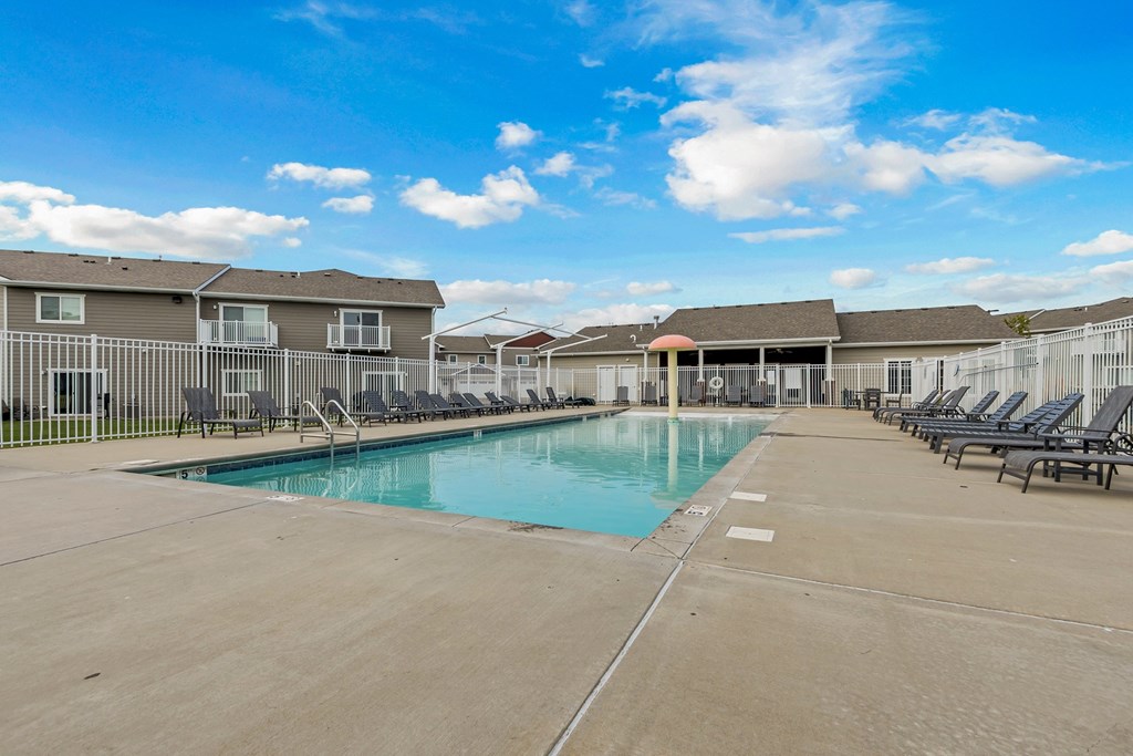 A large swimming pool surrounded by lounge chairs and apartment buildings.