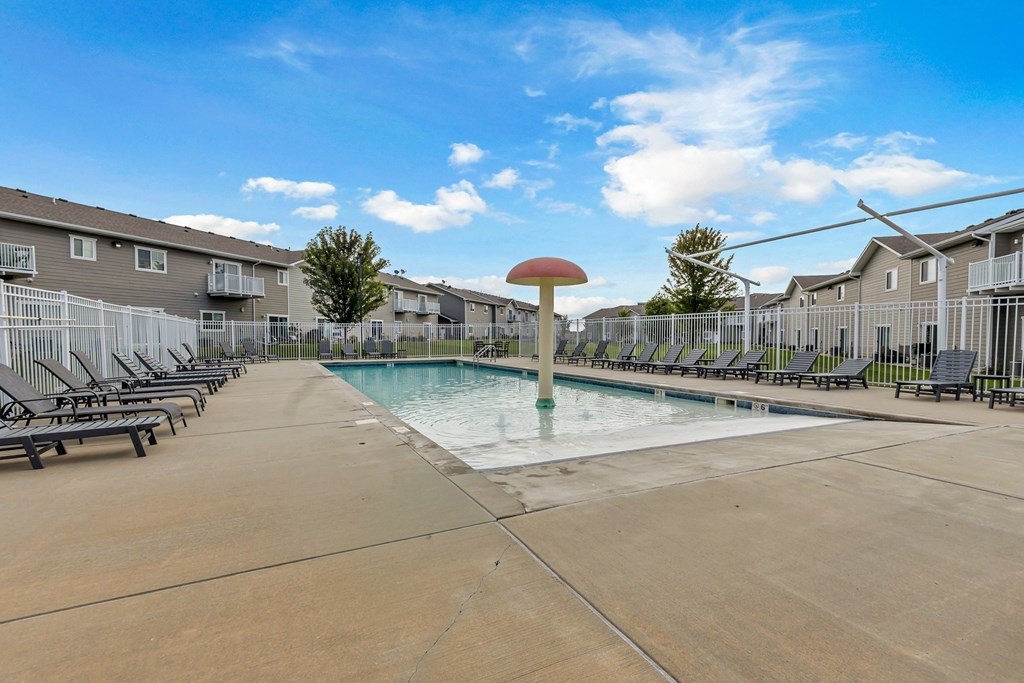 A swimming pool surrounded by lounge chairs and apartment buildings.