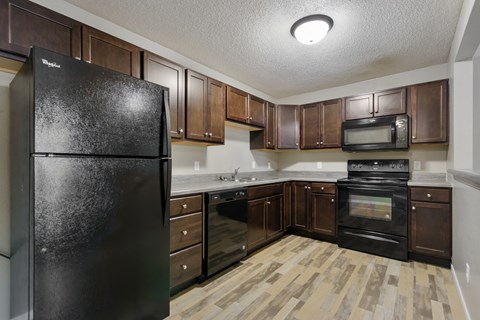 A black refrigerator in a kitchen with wooden floors and brown cabinets.