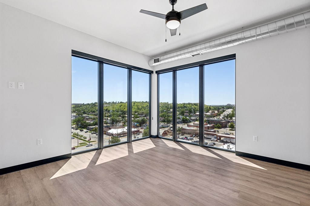 A room with a ceiling fan and large windows overlooking a cityscape.