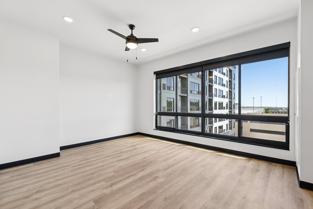A room with a ceiling fan and a large window overlooking a cityscape.