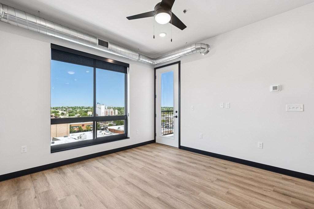 A room with a ceiling fan and a view of the city through the window.