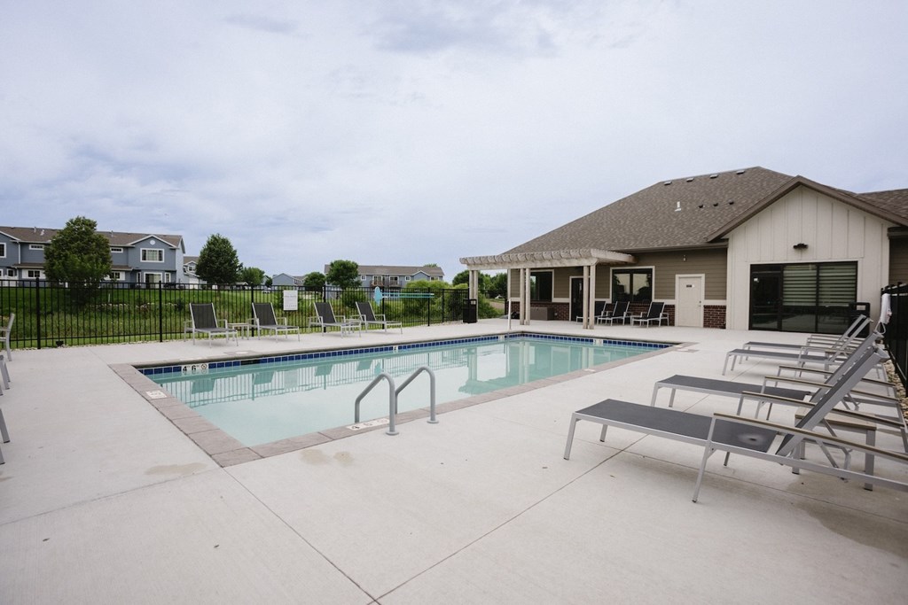 a swimming pool with chairs and a house in the background