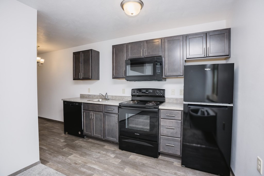 an apartment kitchen with black appliances and dark wood cabinets