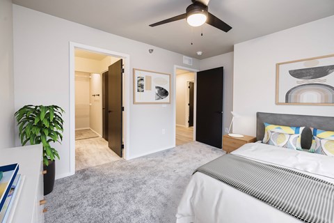 A bedroom with a bed, a ceiling fan, and a painting on the wall.