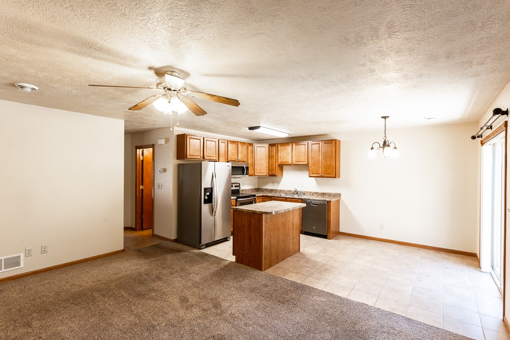 an empty living room with a kitchen and a ceiling fan