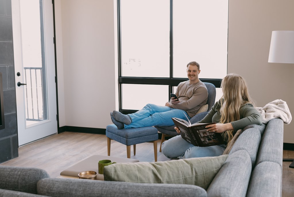 A man and a woman are sitting on a couch and a chair respectively, reading a book together.