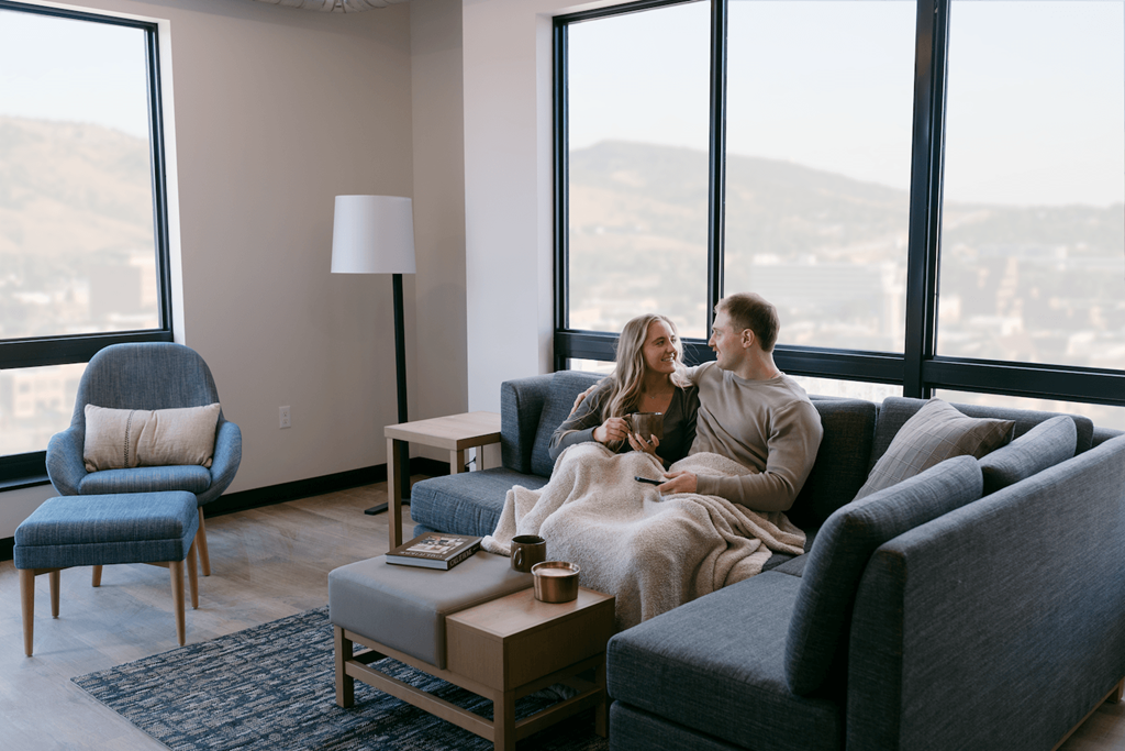 A couple is sitting on a couch in a living room with a view of the city.