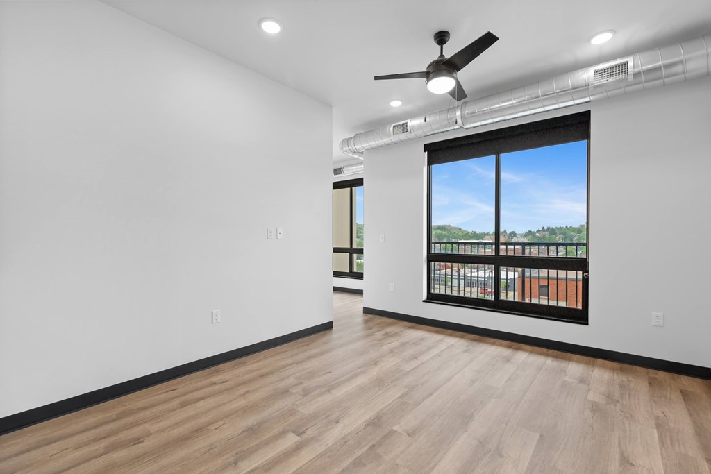 A room with a ceiling fan and a window overlooking a balcony.