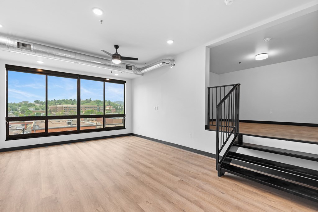 A room with a wooden floor, a staircase, and a ceiling fan.