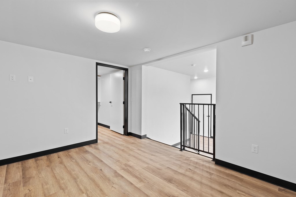 A room with a wooden floor and a white wall with a doorway leading to another room.