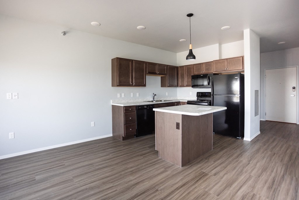 an empty kitchen with wood flooring and a black refrigerator