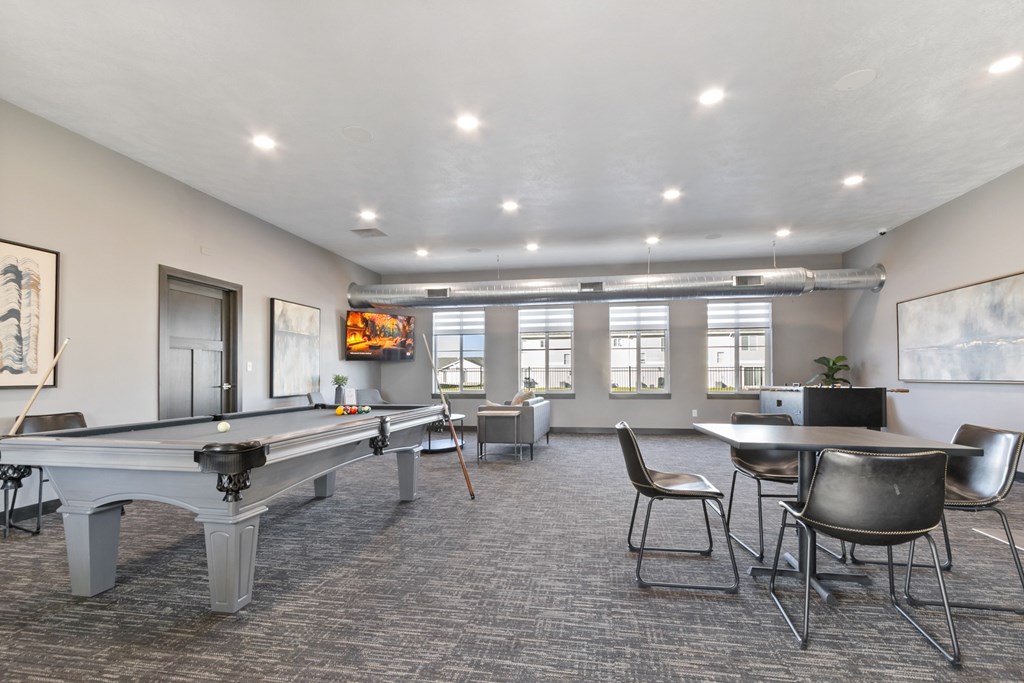 A room with a pool table, chairs, and a TV.
