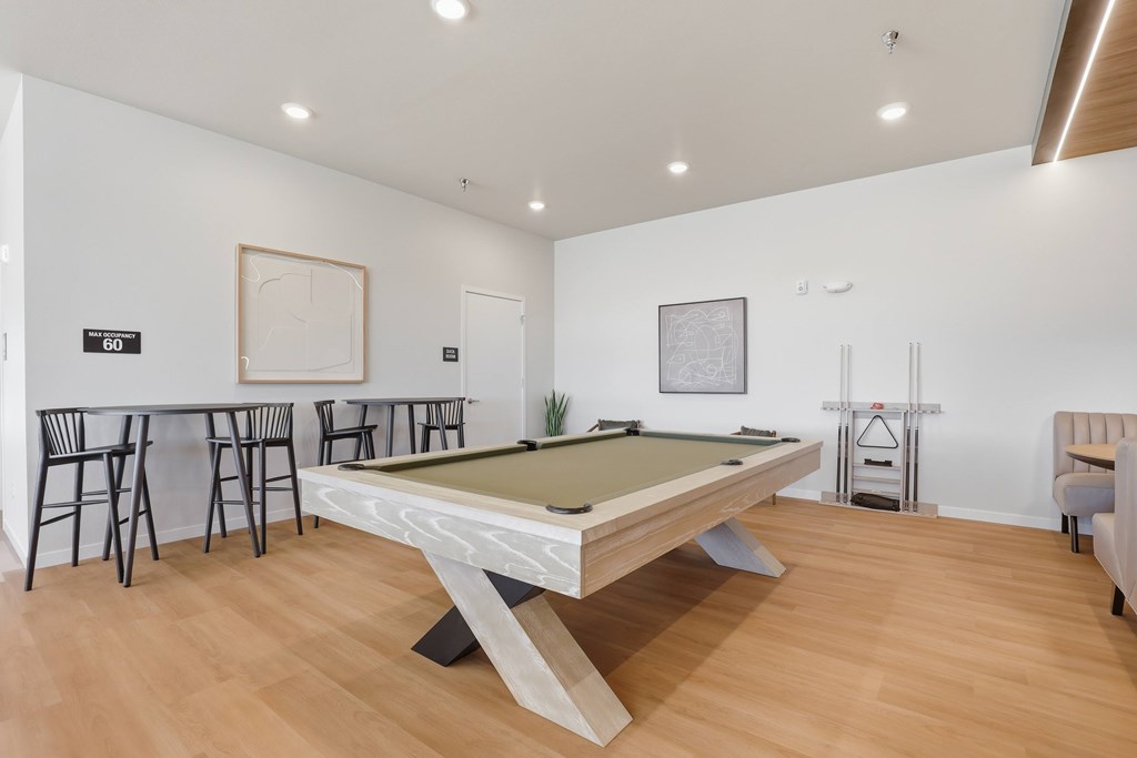 A pool table is in the middle of a room with a bar and chairs.