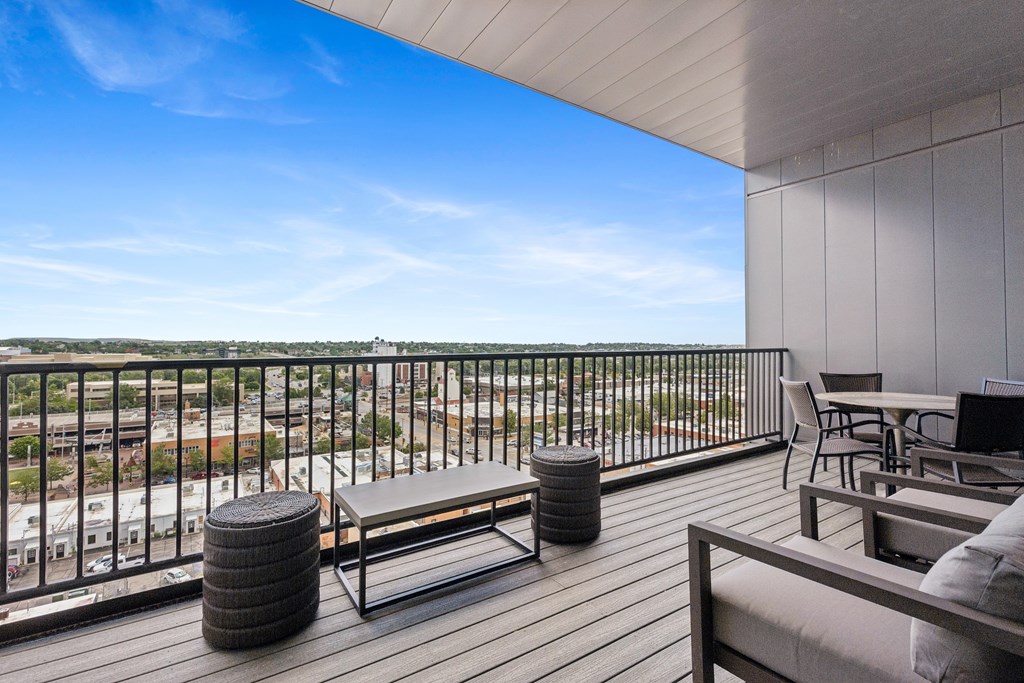A balcony with a bench, table, and chairs overlooking a cityscape.