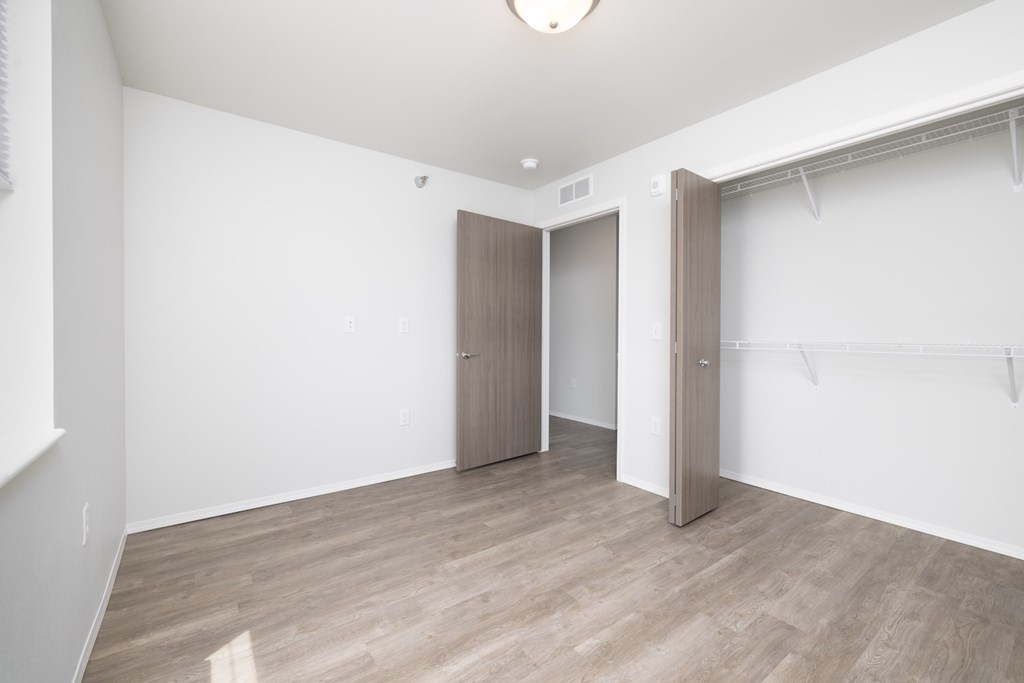 A room with a wooden floor and a white wall with a door and a closet.