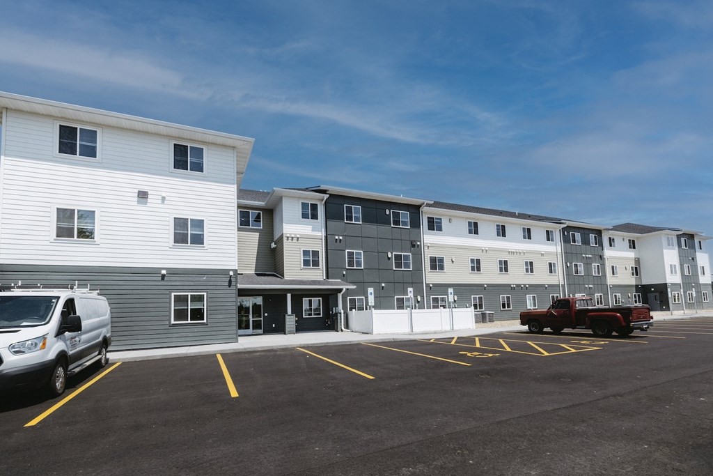 A parking lot with a white van and a red truck parked in front of a building.