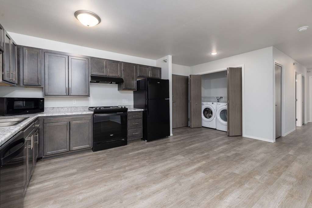 A kitchen with black appliances and wooden floors.