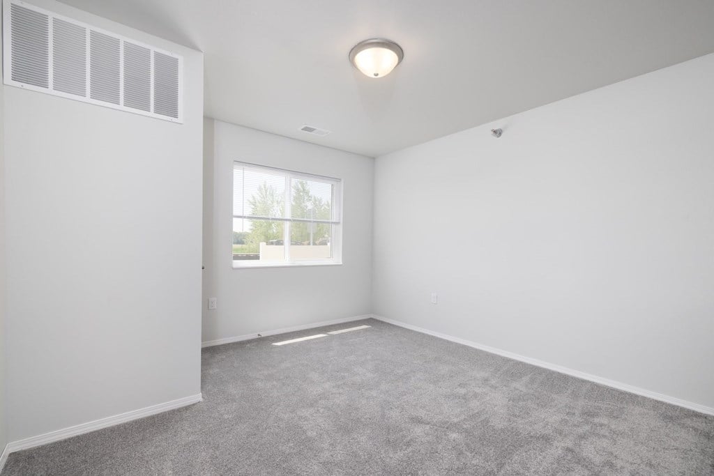 A room with a grey carpet and a window.