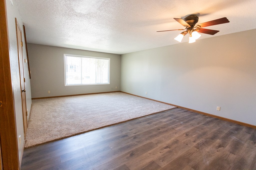 the spacious living room with hardwood flooring and a ceiling fan