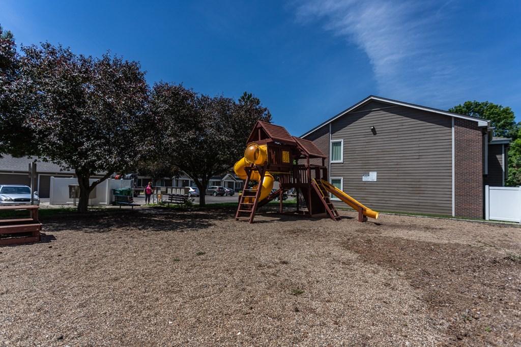 a playground with a yellow swing set in front of a house